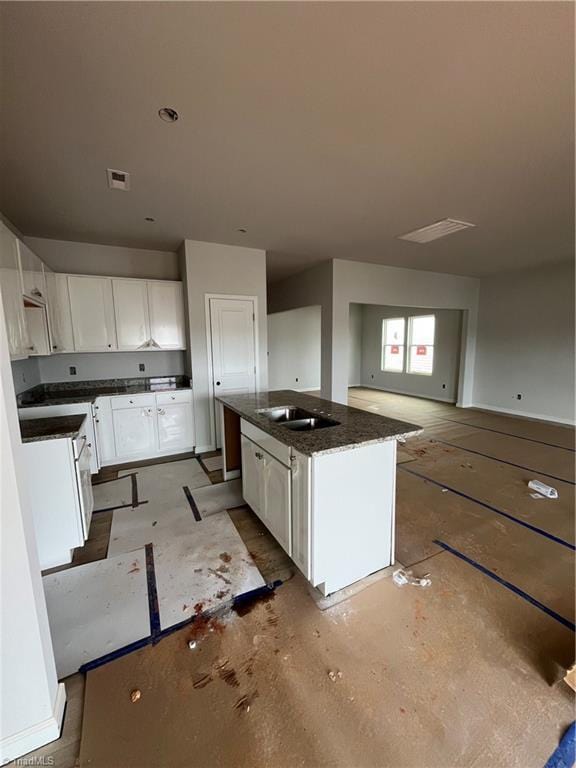 kitchen featuring visible vents, a kitchen island, dark stone countertops, white cabinetry, and a sink