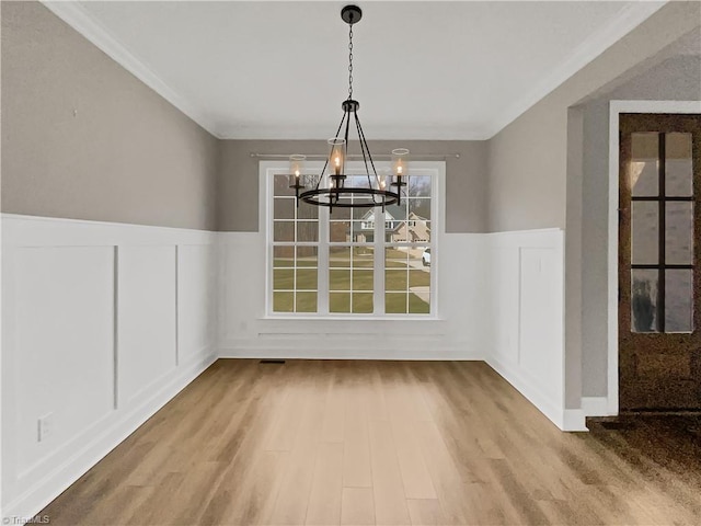 unfurnished dining area featuring an inviting chandelier, ornamental molding, wood finished floors, and wainscoting