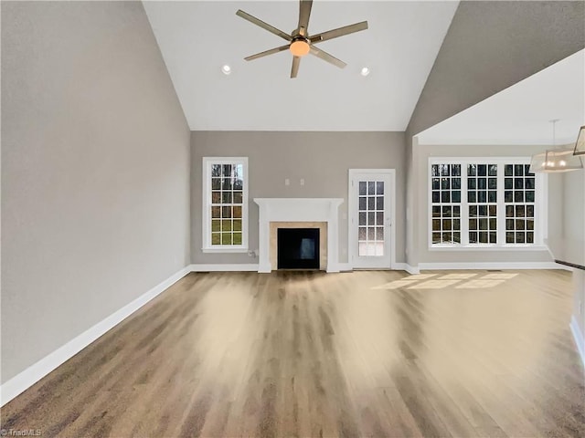 unfurnished living room with high vaulted ceiling, ceiling fan with notable chandelier, wood finished floors, a fireplace, and baseboards