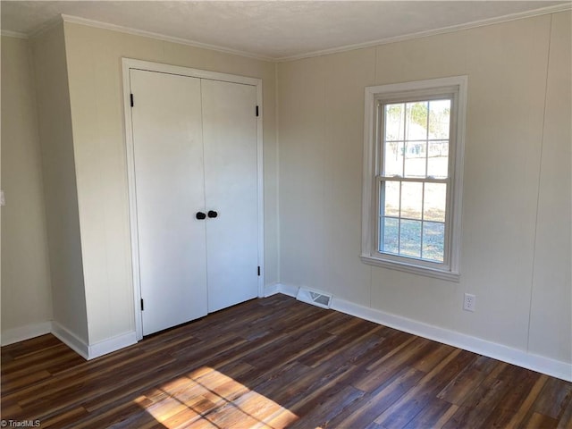 unfurnished bedroom with crown molding, dark wood-type flooring, and a closet