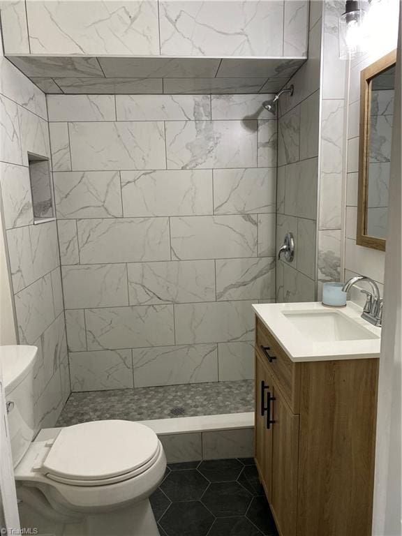 bathroom featuring tile patterned flooring, vanity, toilet, and tiled shower