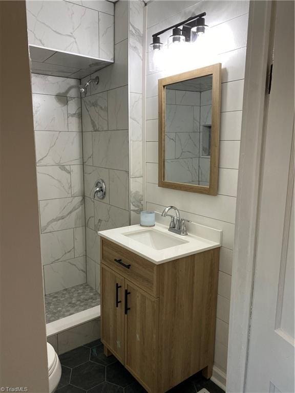 bathroom featuring tile patterned floors, vanity, toilet, and a tile shower