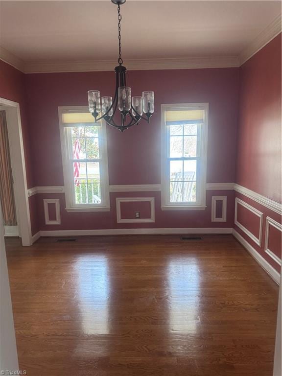 unfurnished room with an inviting chandelier, wood finished floors, and ornamental molding