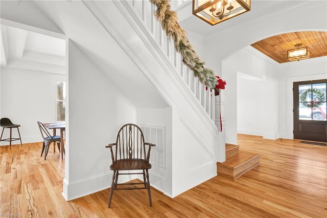 entrance foyer with a chandelier, crown molding, wooden ceiling, and light wood-type flooring