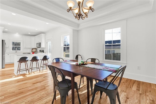 dining area with light hardwood / wood-style floors, a raised ceiling, ornamental molding, and an inviting chandelier