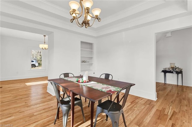 dining room with a notable chandelier, light hardwood / wood-style floors, a raised ceiling, and ornamental molding