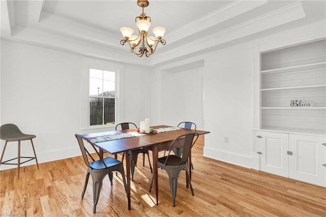 dining room with a raised ceiling, a chandelier, ornamental molding, and light wood-type flooring