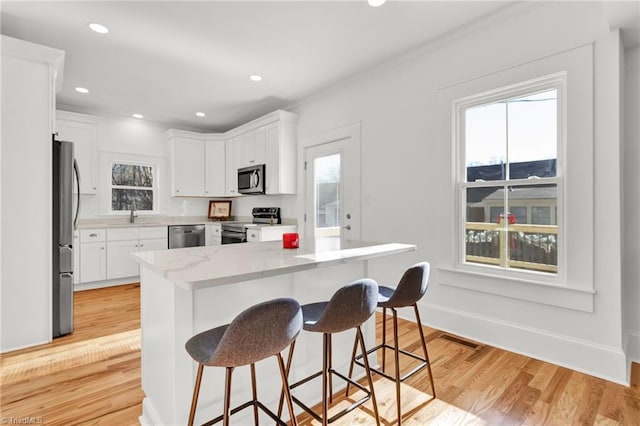 kitchen with appliances with stainless steel finishes, light wood-type flooring, light stone counters, a breakfast bar, and white cabinets