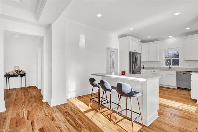 kitchen with stainless steel appliances, a kitchen island, a kitchen bar, white cabinets, and light wood-type flooring