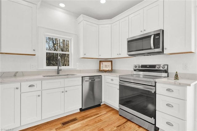 kitchen with appliances with stainless steel finishes, light stone counters, sink, light hardwood / wood-style floors, and white cabinetry