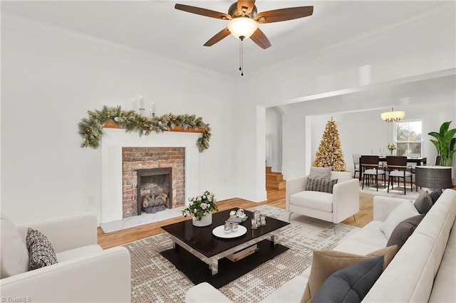 living room with a fireplace, ornamental molding, ceiling fan with notable chandelier, and light wood-type flooring