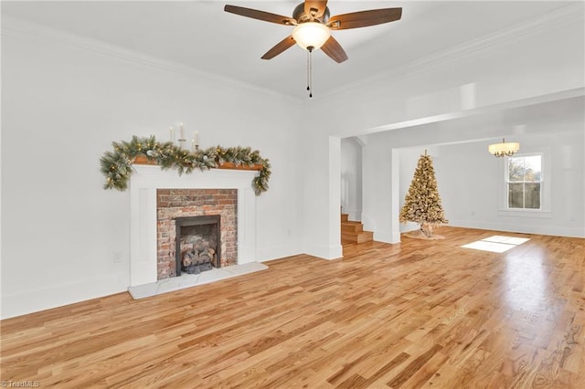 unfurnished living room with ceiling fan with notable chandelier, light wood-type flooring, a brick fireplace, and crown molding