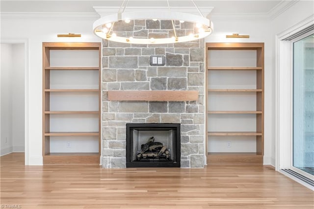 unfurnished living room with built in shelves, ornamental molding, wood finished floors, a stone fireplace, and baseboards