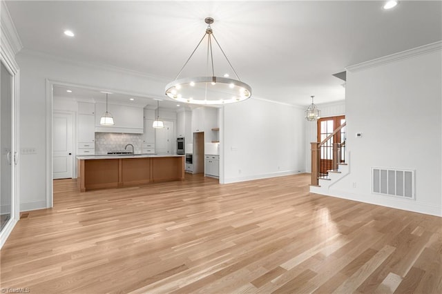 unfurnished living room with visible vents, a notable chandelier, light wood-style flooring, stairway, and crown molding