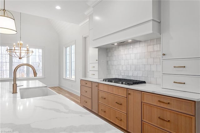 kitchen featuring light stone countertops, stainless steel gas cooktop, lofted ceiling, a sink, and hanging light fixtures