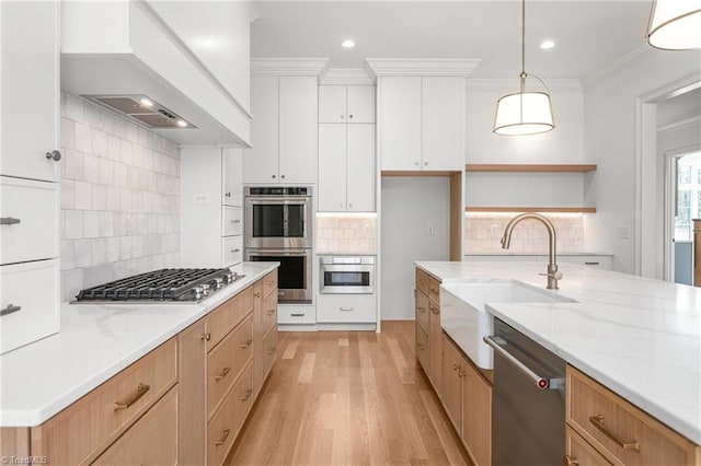 kitchen featuring ornamental molding, a sink, light wood-style floors, appliances with stainless steel finishes, and custom exhaust hood