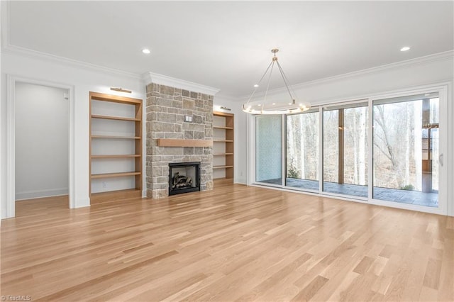 unfurnished living room with built in shelves, light wood-style floors, a stone fireplace, an inviting chandelier, and crown molding
