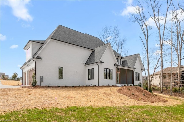rear view of house with stucco siding, a garage, driveway, and roof with shingles