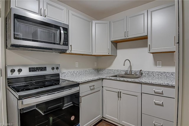 kitchen with white cabinets, appliances with stainless steel finishes, light stone countertops, and sink