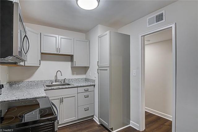 kitchen with light stone countertops, stove, dark wood-type flooring, and sink