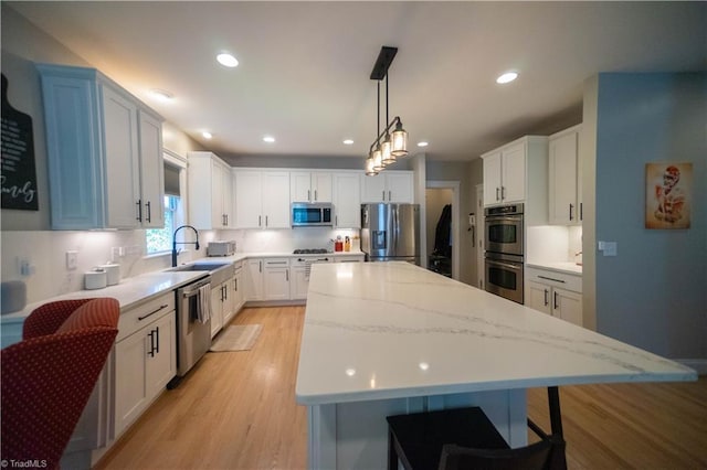 kitchen with appliances with stainless steel finishes, sink, pendant lighting, a center island, and white cabinetry