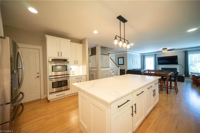 kitchen with white cabinetry, hanging light fixtures, stainless steel appliances, light hardwood / wood-style flooring, and a kitchen island