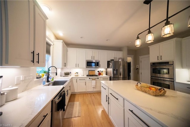 kitchen featuring light wood-type flooring, stainless steel appliances, sink, white cabinets, and hanging light fixtures