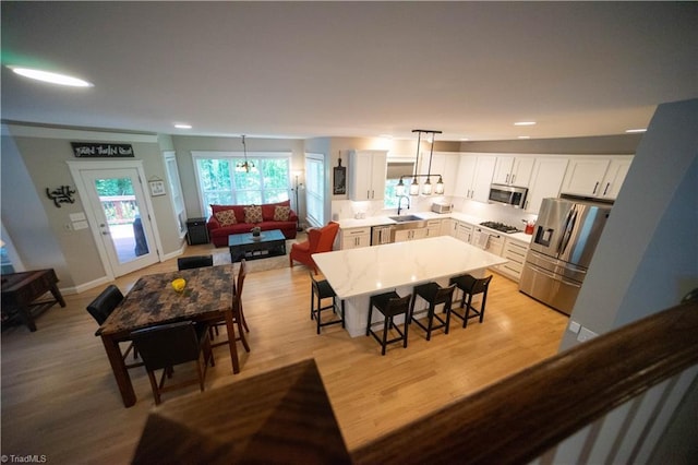 kitchen with white cabinetry, sink, hanging light fixtures, a breakfast bar area, and appliances with stainless steel finishes