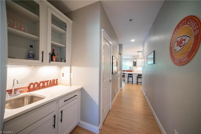 bar with backsplash, sink, white cabinets, and light hardwood / wood-style floors