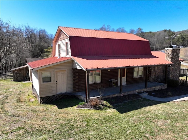 rear view of house with a gambrel roof, a porch, a chimney, metal roof, and a yard