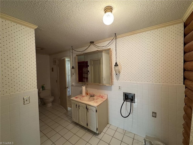 bathroom with a textured ceiling, wainscoting, and wallpapered walls