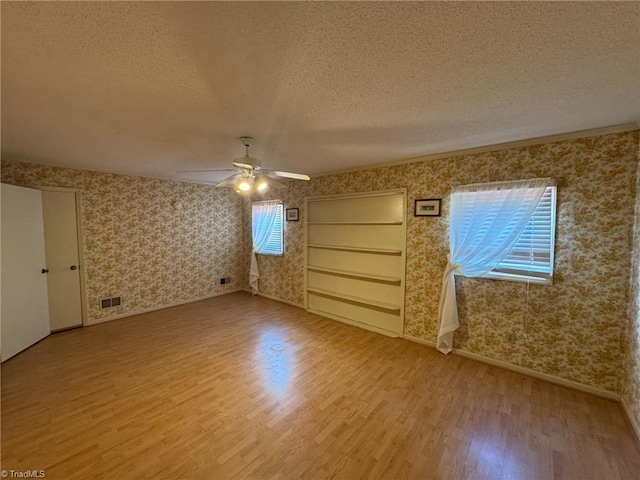 empty room featuring a textured ceiling, wood finished floors, and wallpapered walls