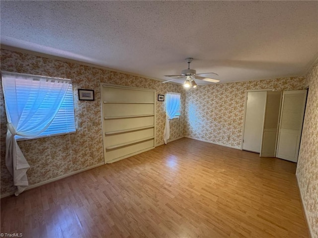 interior space with wallpapered walls, a textured ceiling, light wood finished floors, baseboards, and ceiling fan