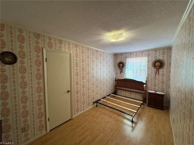 bedroom with ornamental molding, a textured ceiling, wood finished floors, wallpapered walls, and baseboards