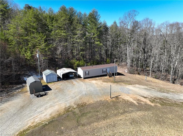 view of front of property with an outbuilding, a wooded view, driveway, and a carport