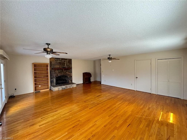 unfurnished living room featuring a stone fireplace, light wood-style flooring, a textured ceiling, and ceiling fan