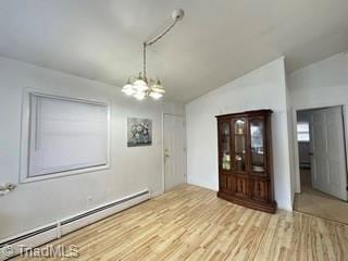 unfurnished dining area featuring a baseboard heating unit, a chandelier, vaulted ceiling, and wood finished floors