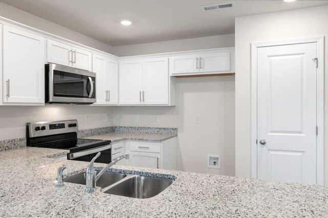 kitchen with white cabinets, stainless steel appliances, light stone countertops, and sink