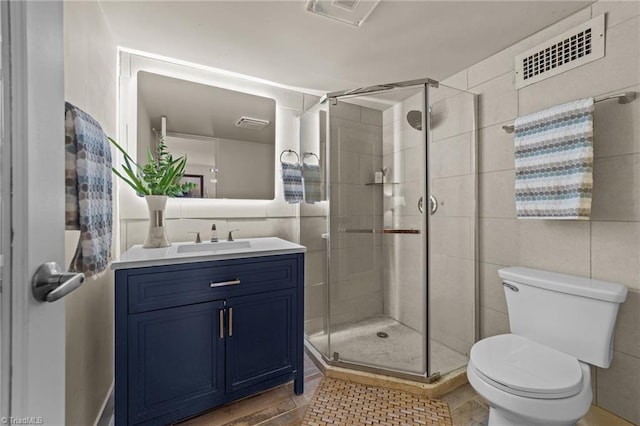 bathroom with tile walls, vanity, toilet, and a shower with shower door