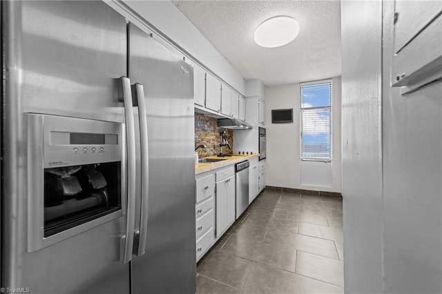 kitchen with white cabinets, backsplash, stainless steel appliances, dark tile patterned floors, and sink