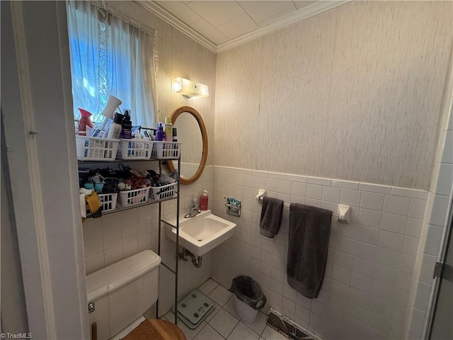 bathroom featuring tile patterned floors, toilet, sink, crown molding, and tile walls