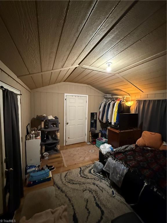 bedroom with vaulted ceiling, wooden ceiling, and wood walls