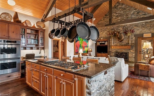 kitchen with wood ceiling, an island with sink, appliances with stainless steel finishes, a fireplace, and dark wood-style floors