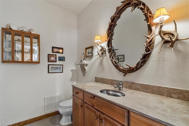 bathroom featuring visible vents, toilet, baseboards, vanity, and a textured wall