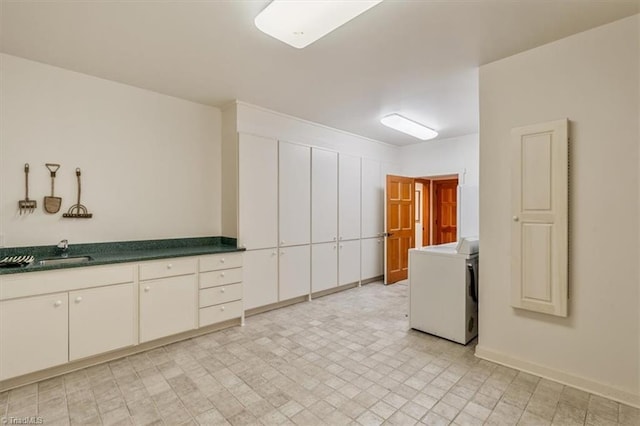 kitchen with dark countertops, washer / clothes dryer, light floors, and a sink