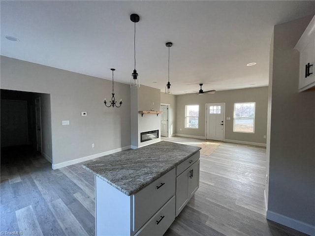 kitchen with light wood-type flooring, a kitchen island, white cabinetry, and baseboards