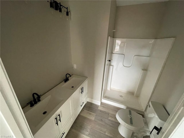 bathroom featuring baseboards, toilet, wood finished floors, a walk in shower, and a sink