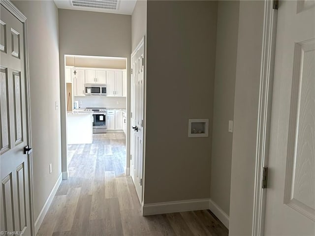 corridor with light wood-style floors, baseboards, and visible vents