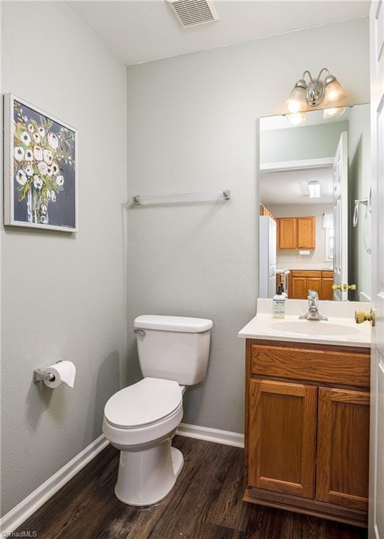 bathroom with vanity, wood finished floors, baseboards, visible vents, and toilet