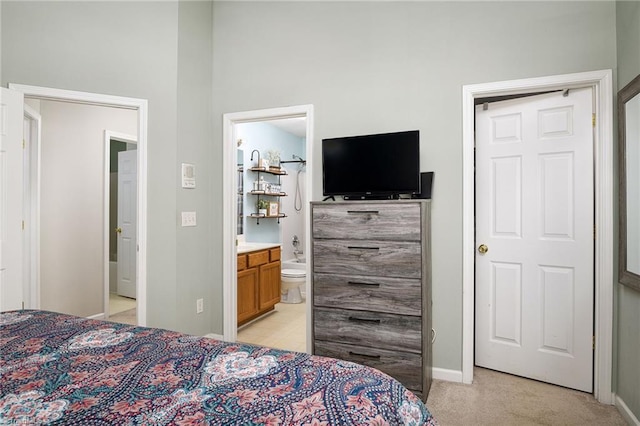 bedroom with baseboards, light carpet, and ensuite bathroom